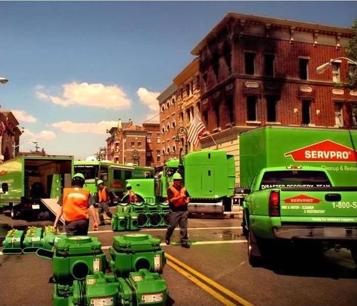 Green trucks and men moving equipment towards a job downtonw.